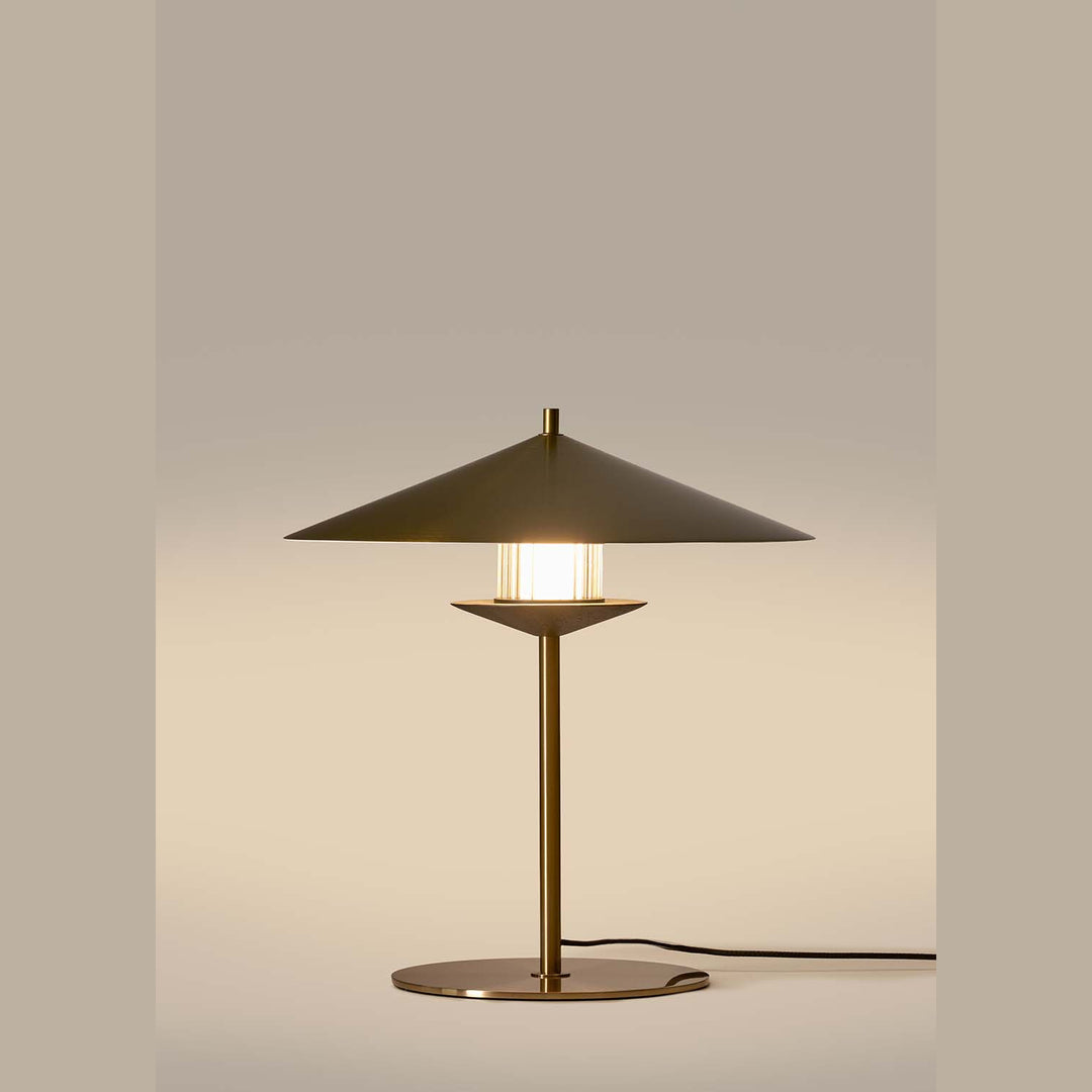 Gehit Table Lamp lit, warm glow through the striped glass beneath its brass cone shade