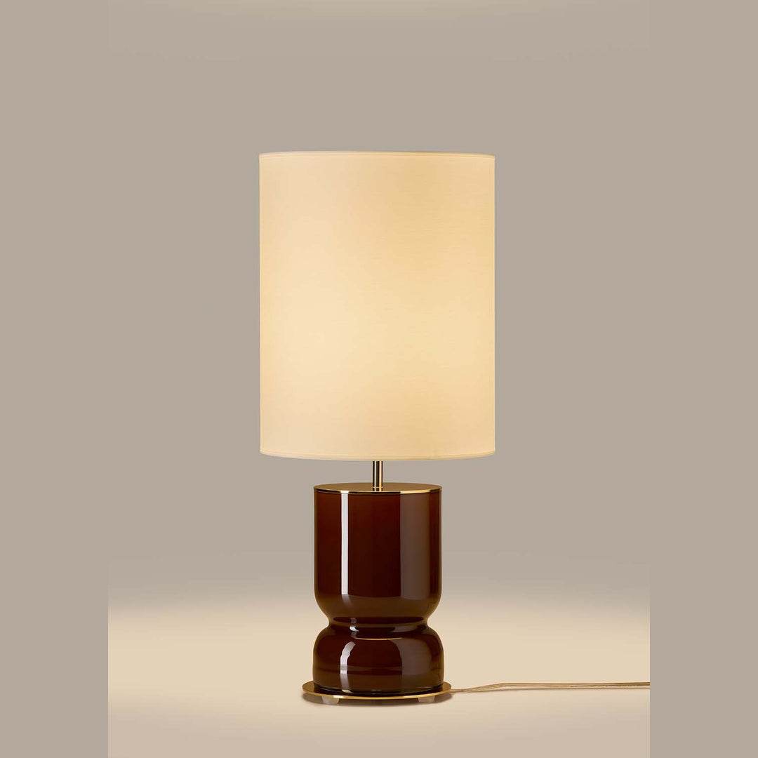 Glossy chocolate brown glass table lamp with tall cream shade, unlit, on a taupe backdrop