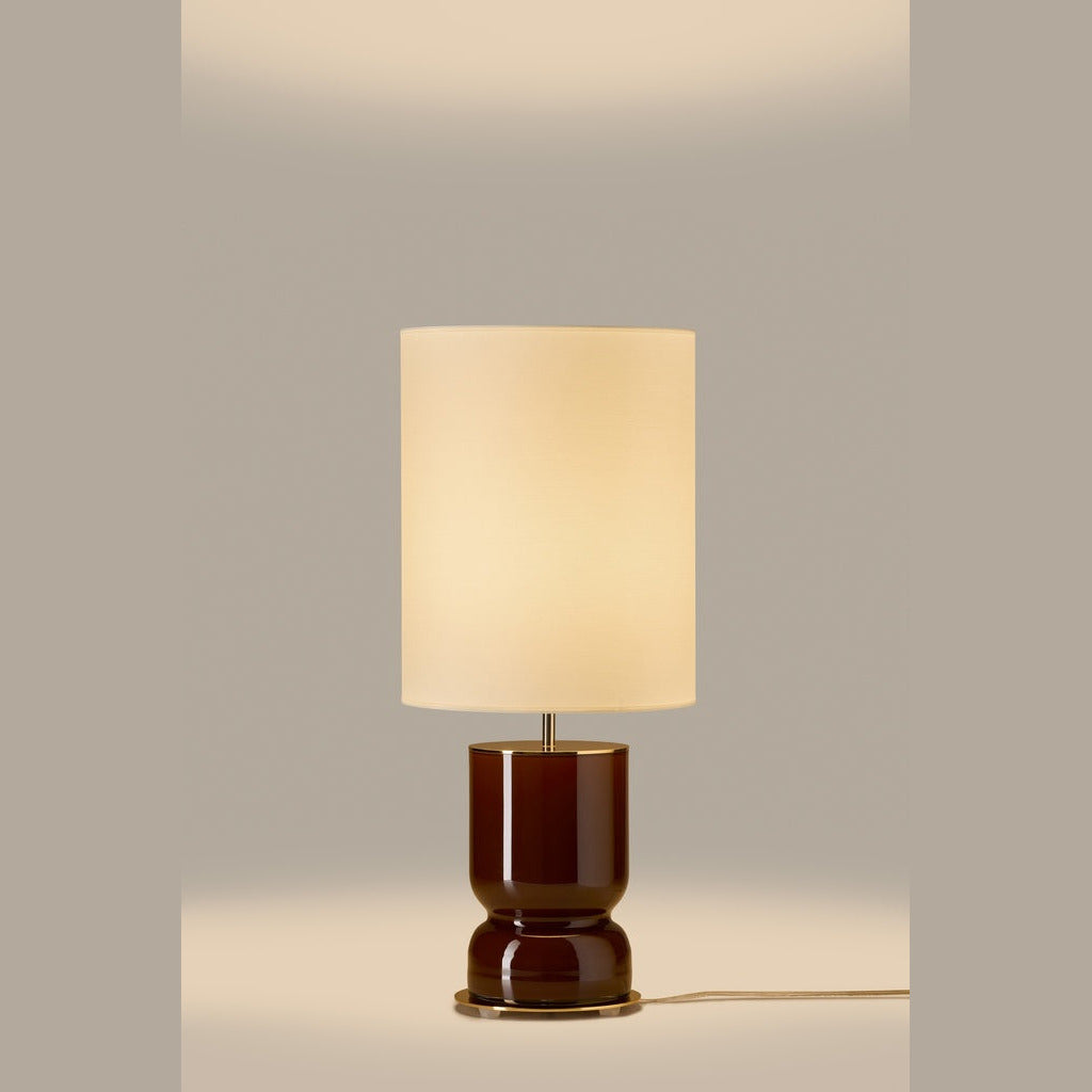 Lit table lamp with glossy chocolate brown glass base and glowing cream drum shade