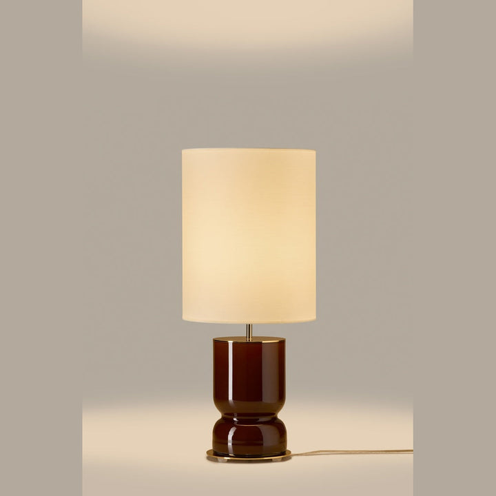 Lit table lamp with glossy chocolate brown glass base and glowing cream drum shade