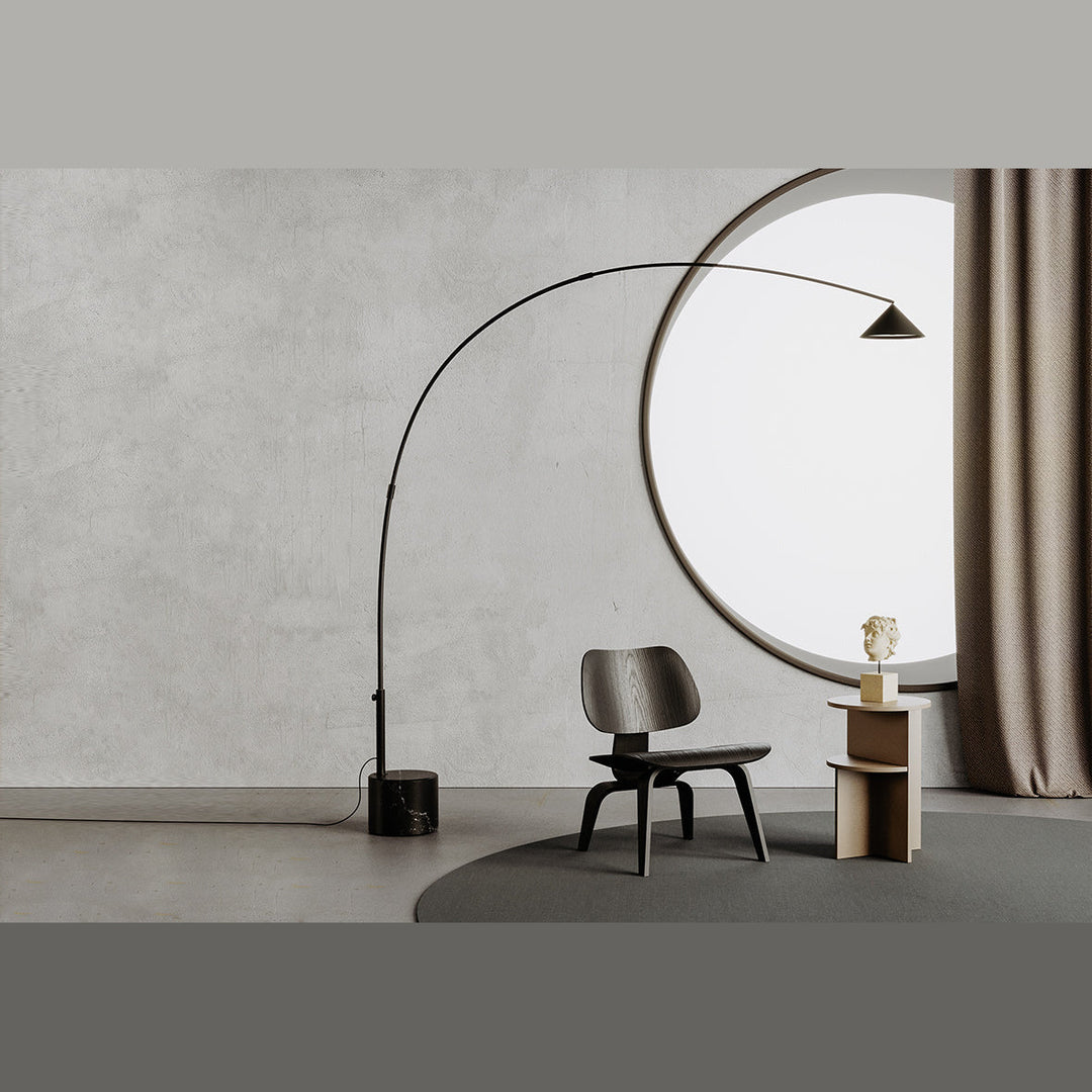 Arc floor lamp with brass shade beside a dark wood lounge chair in a grey room with round window
