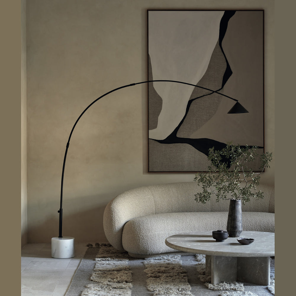 Black arc lamp reaching over a white curved sofa and round coffee table beneath abstract art