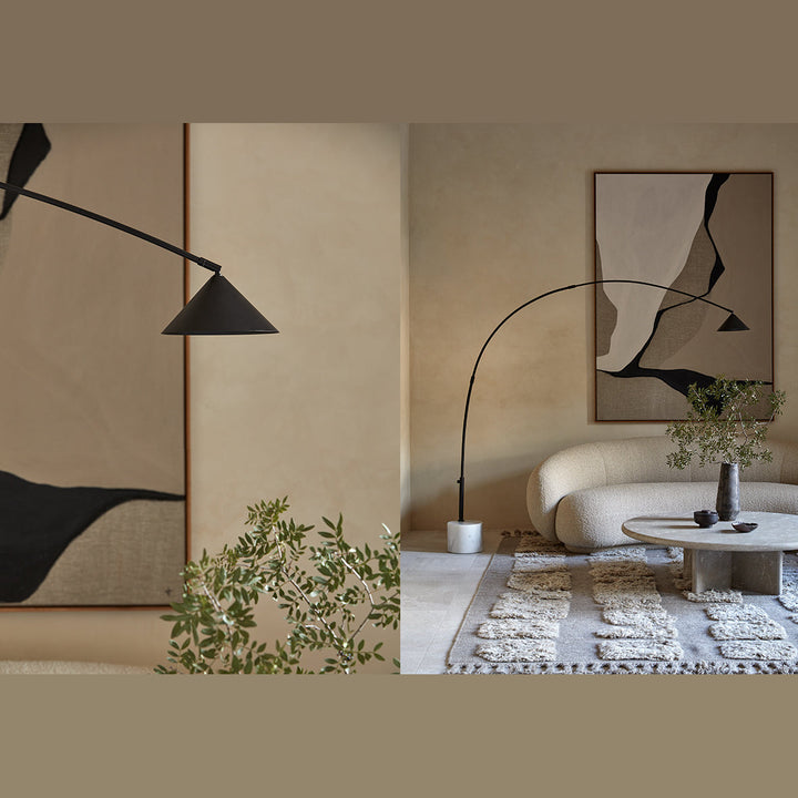 Black arc floor lamp with cone shade arching over a curved boucle sofa and stone coffee table