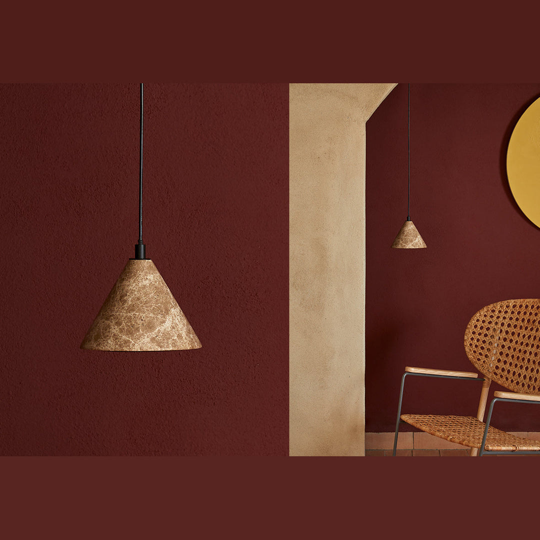 Iconic Pendant Lamp in marble against a deep red wall beside a rattan chair