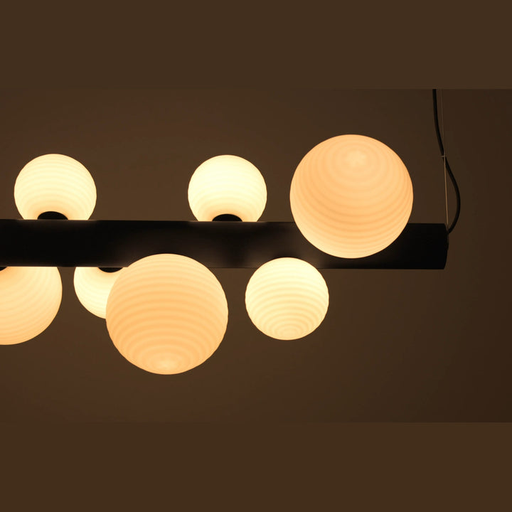 Close-up of horizontal Lera Pendant Lamp lit, ribbed opal globes on a dark bar