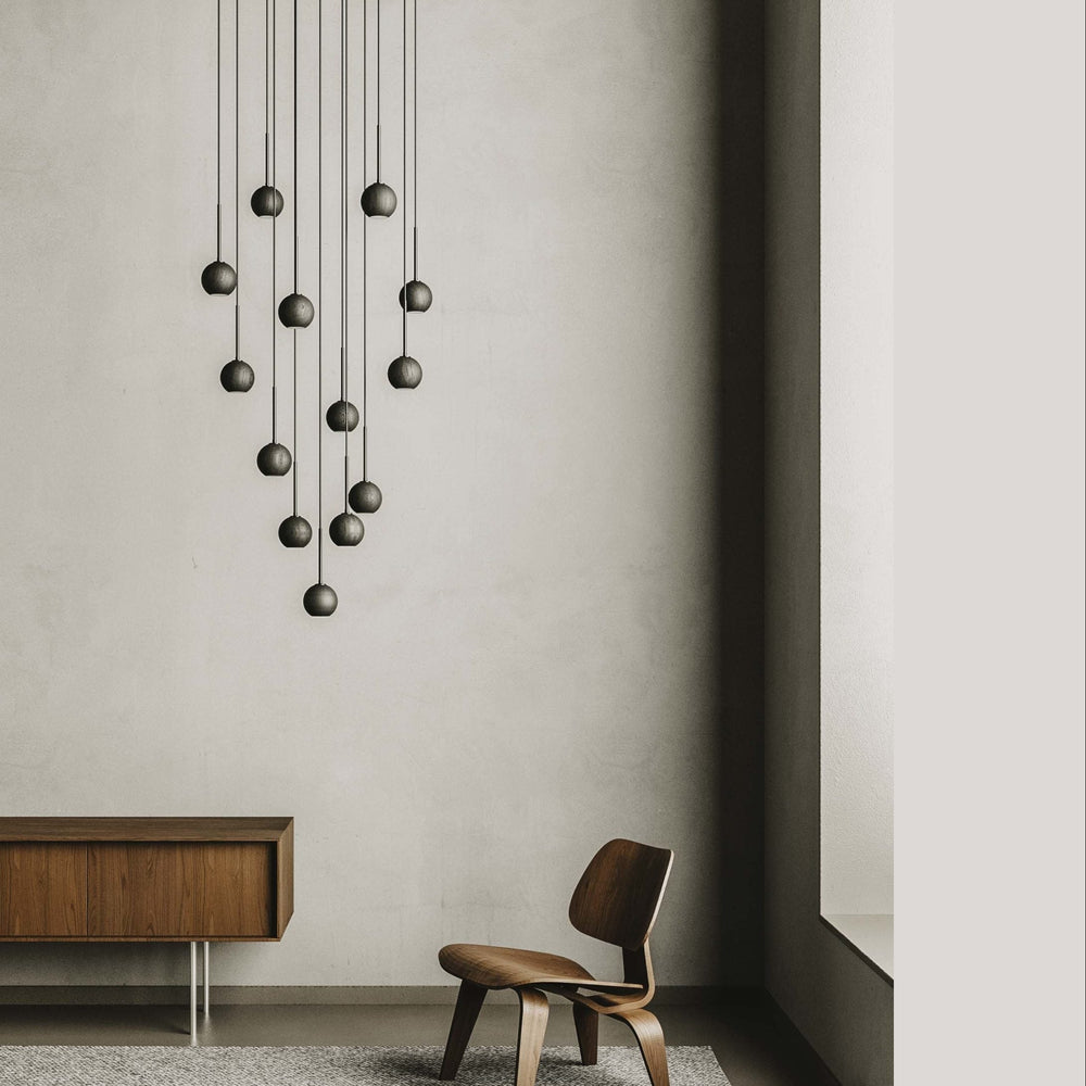 Pendant cluster over a wood sideboard and moulded plywood lounge chair in a tall grey room