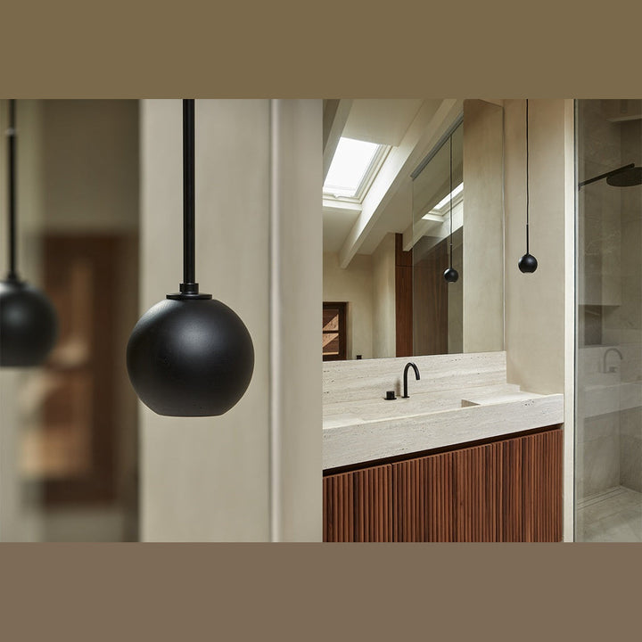Lita Pendant Lamp close-up of a matt black sphere with a stone bathroom vanity behind