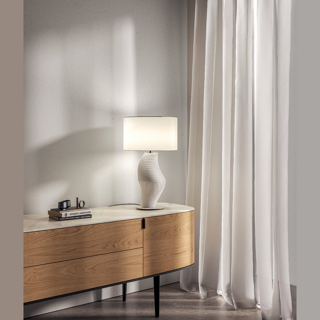Luet Table Lamp in white, lit on an oak sideboard next to long white curtains