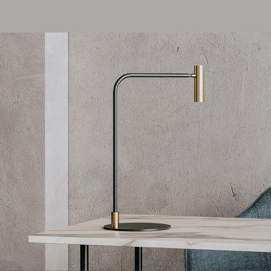 Black and brass desk lamp on a marble-top desk against a textured plaster wall, teal chair beside