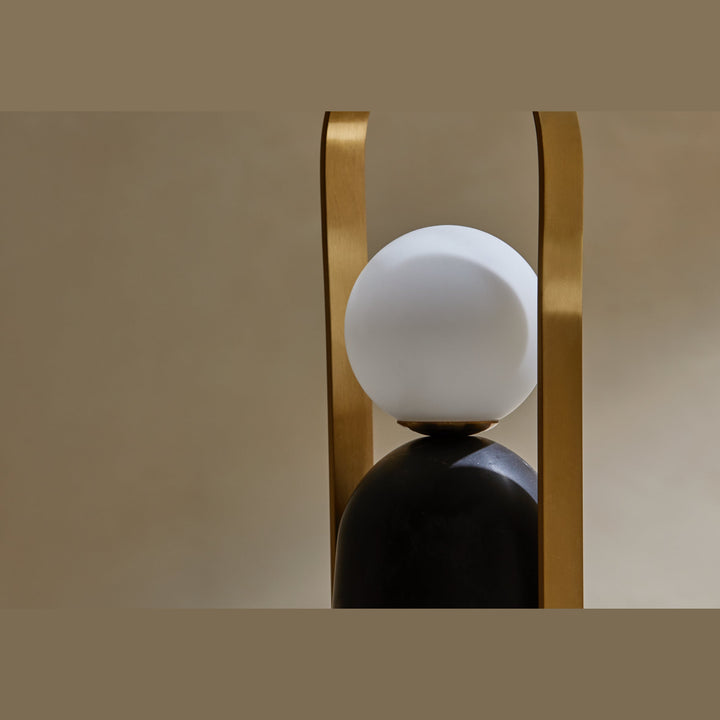 Close-up of the Nano Portable Table Lamp opal globe framed by its brass handle above black marble