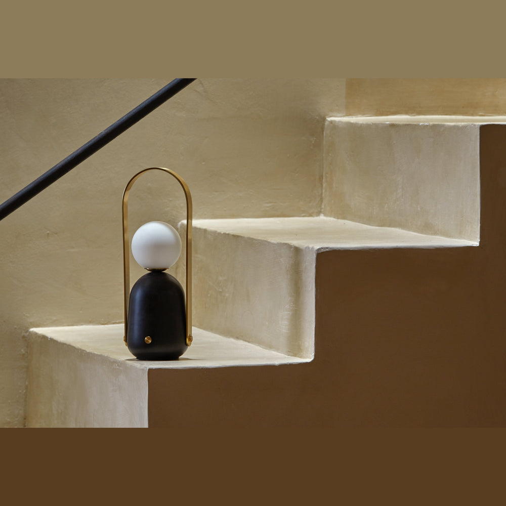 Nano Portable Table Lamp resting on a plaster staircase step beside a black handrail