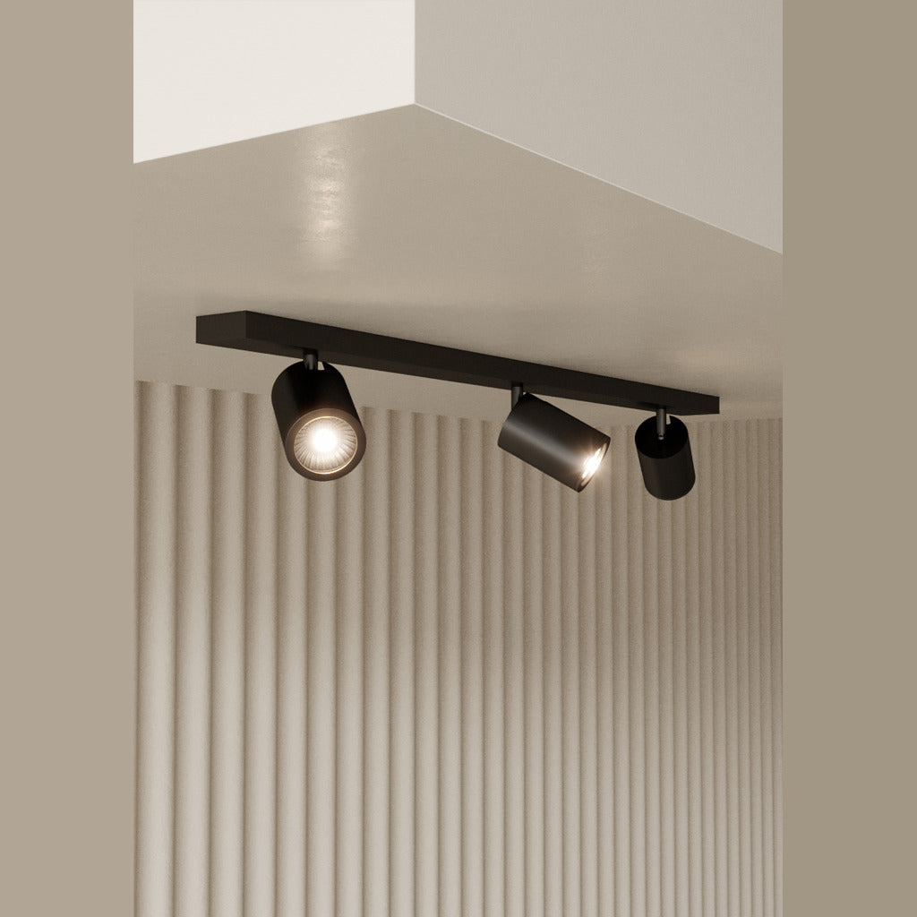 Noon Spot, Triple, lit, three spotlights on a black bar above a fluted beige wall