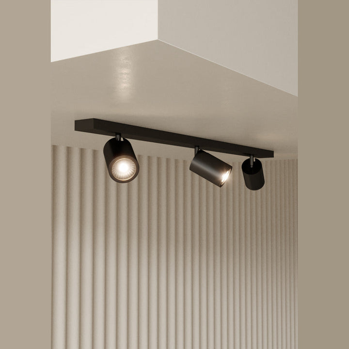 Noon Spot, Triple, lit, three spotlights on a black bar above a fluted beige wall