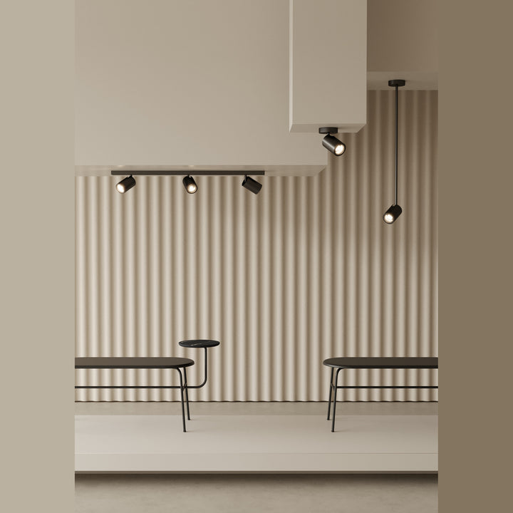 Noon Spots on a ceiling track and a single drop rod above benches against a ribbed wall
