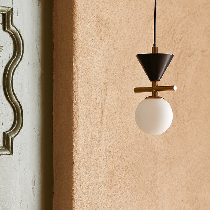 Oneta Pendant Lamp with black cone and gold bar hanging beside a carved plaster panel on a terracotta wall