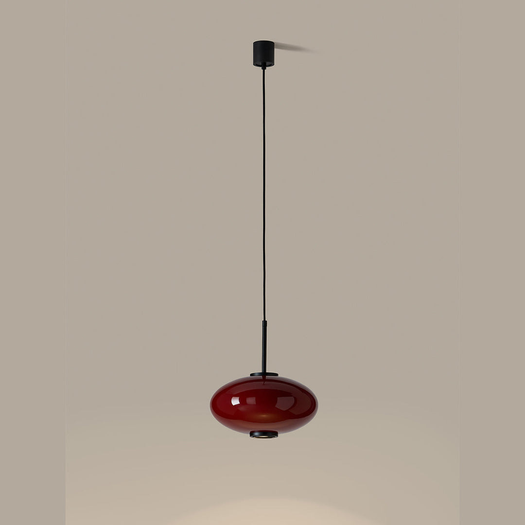 Ovalo Pendant Lamp in red glass, lit and casting a pool of light below