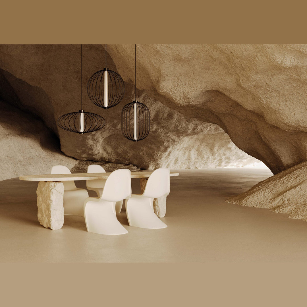 Dark cage pendants lit over a stone table and white chairs in a sculpted cave-like room