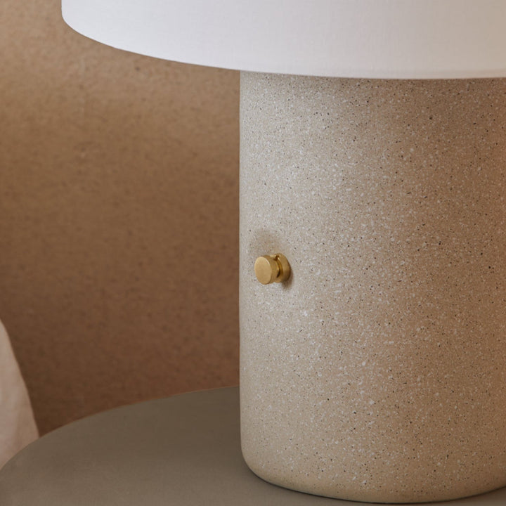 Close-up of the terrazzo base and brass knob on a bedside table next to linen bedding