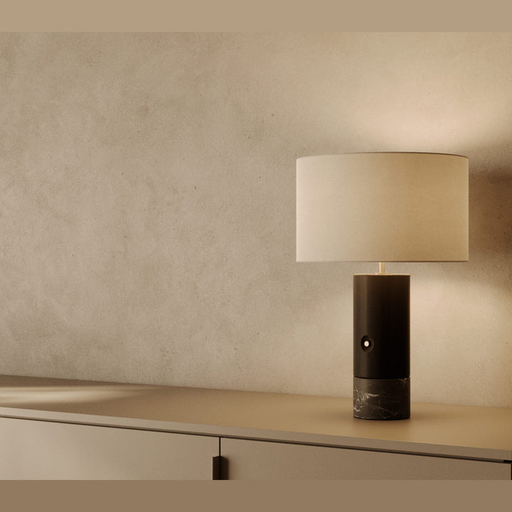 Sano Table Lamp in black wood and black marble with white shade, lit, on a low cabinet