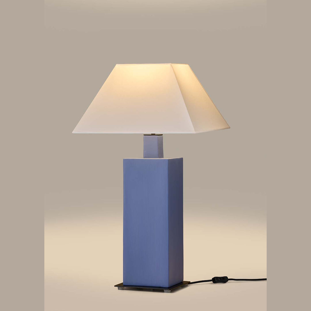 Syal Table Lamp lit, blue ceramic base glowing under a white tapered shade