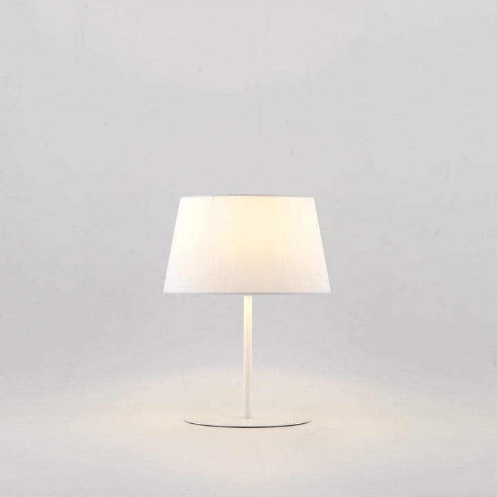 Tex Table Lamp in Matt White with tapered white shade, lit with a warm glow
