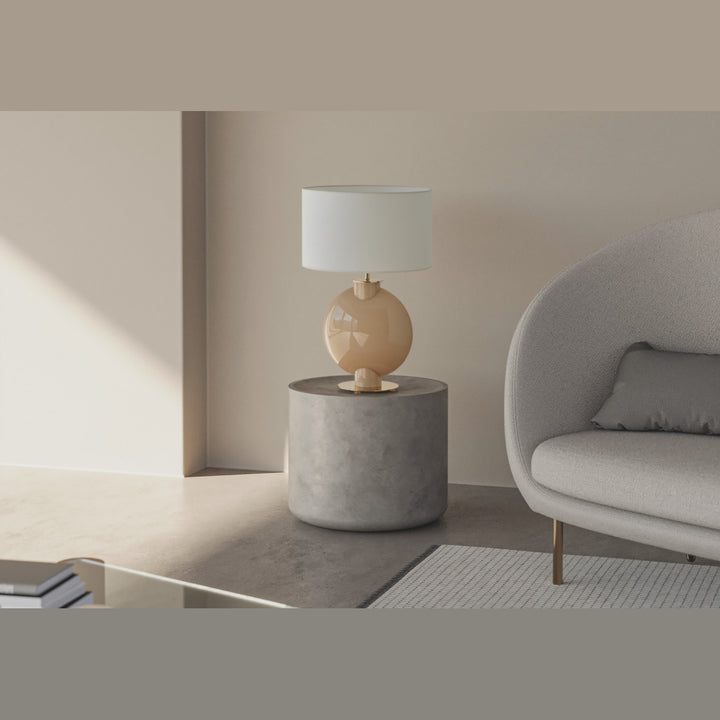 Tilla Table Lamp in nude glass lit on a stone side table beside a curved boucle sofa