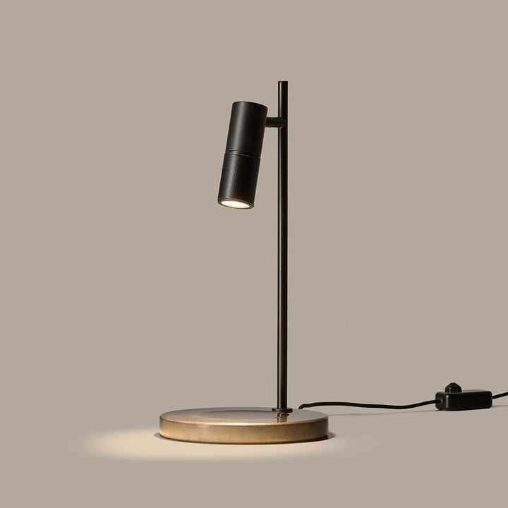Tura C Table Lamp in matt black with aged gold base, lit and casting a pool of light