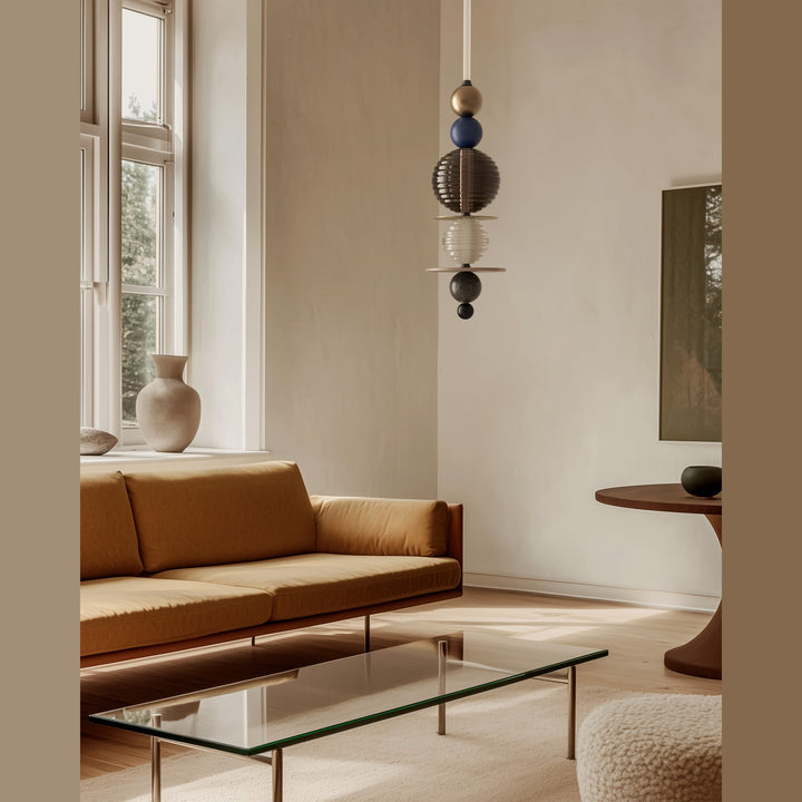 Yma Vertical Pendant Lamp hanging in a bright living room with a tan sofa and glass coffee table