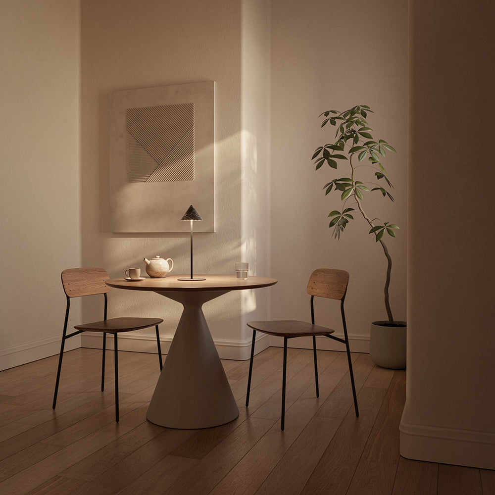 Anza Table Lamp on a round pedestal dining table with a teapot, between two wood chairs in evening light