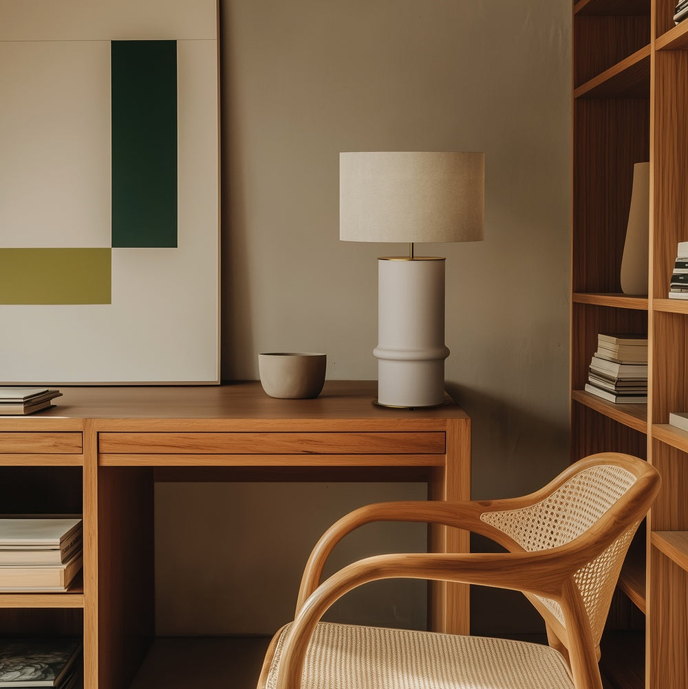Bambu Table Lamp in off-white ceramic with linen shade on a teak desk beside a cane armchair and bookshelves