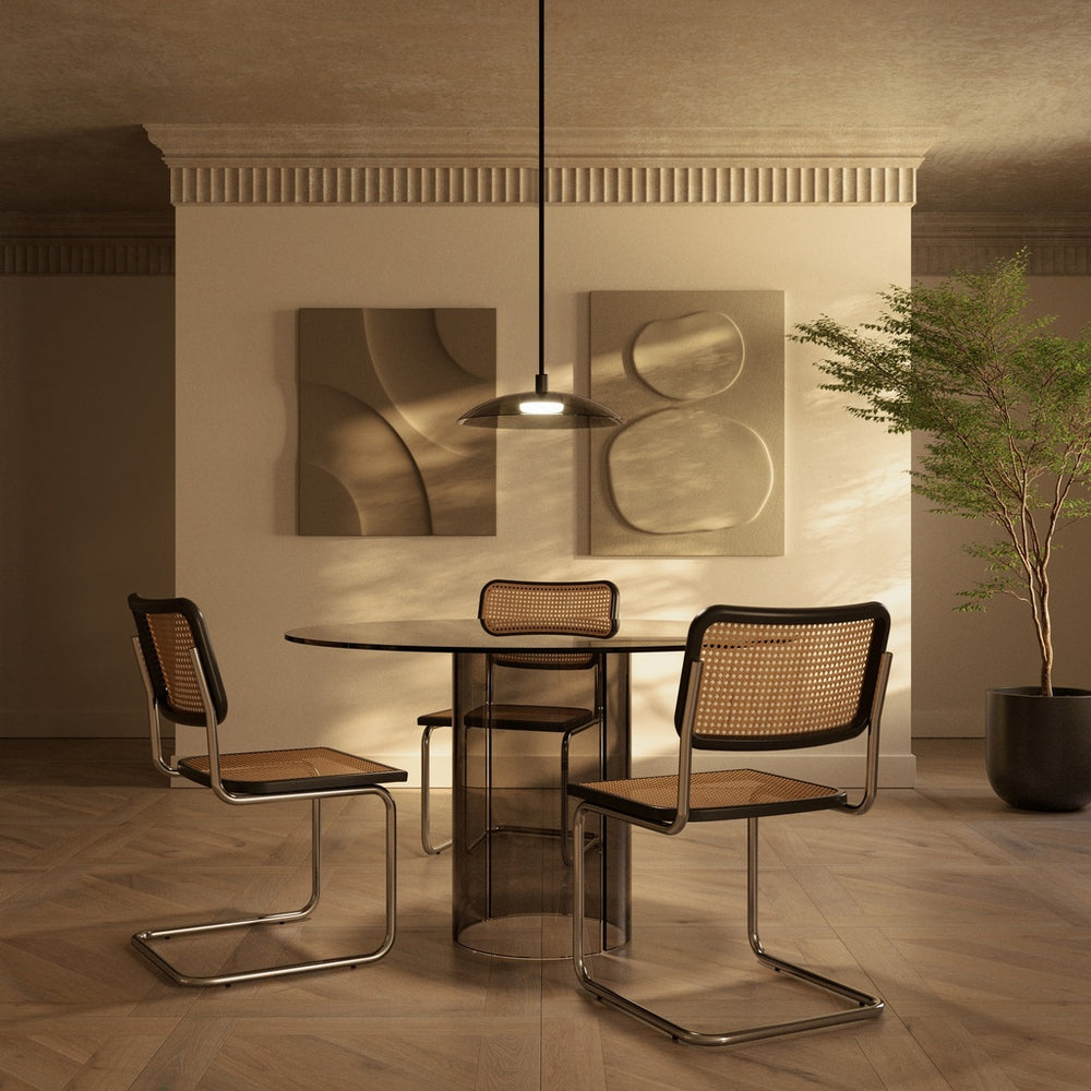 Betty Pendant Lamp lit above a round glass dining table with cane cantilever chairs