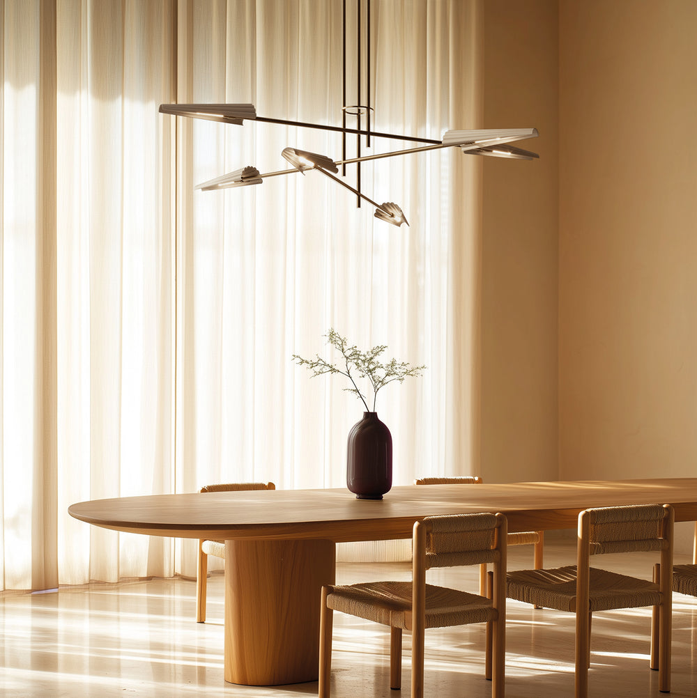 Bion Chandelier lit above a long oak dining table in warm sunlight through sheer curtains