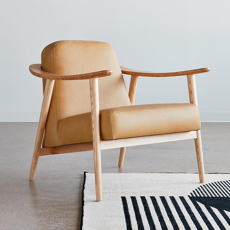 Tan leather armchair with sculpted oak frame, modern mid-century design on striped rug