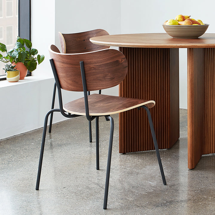 Walnut wood dining chair with black metal frame, modern design beside fluted table