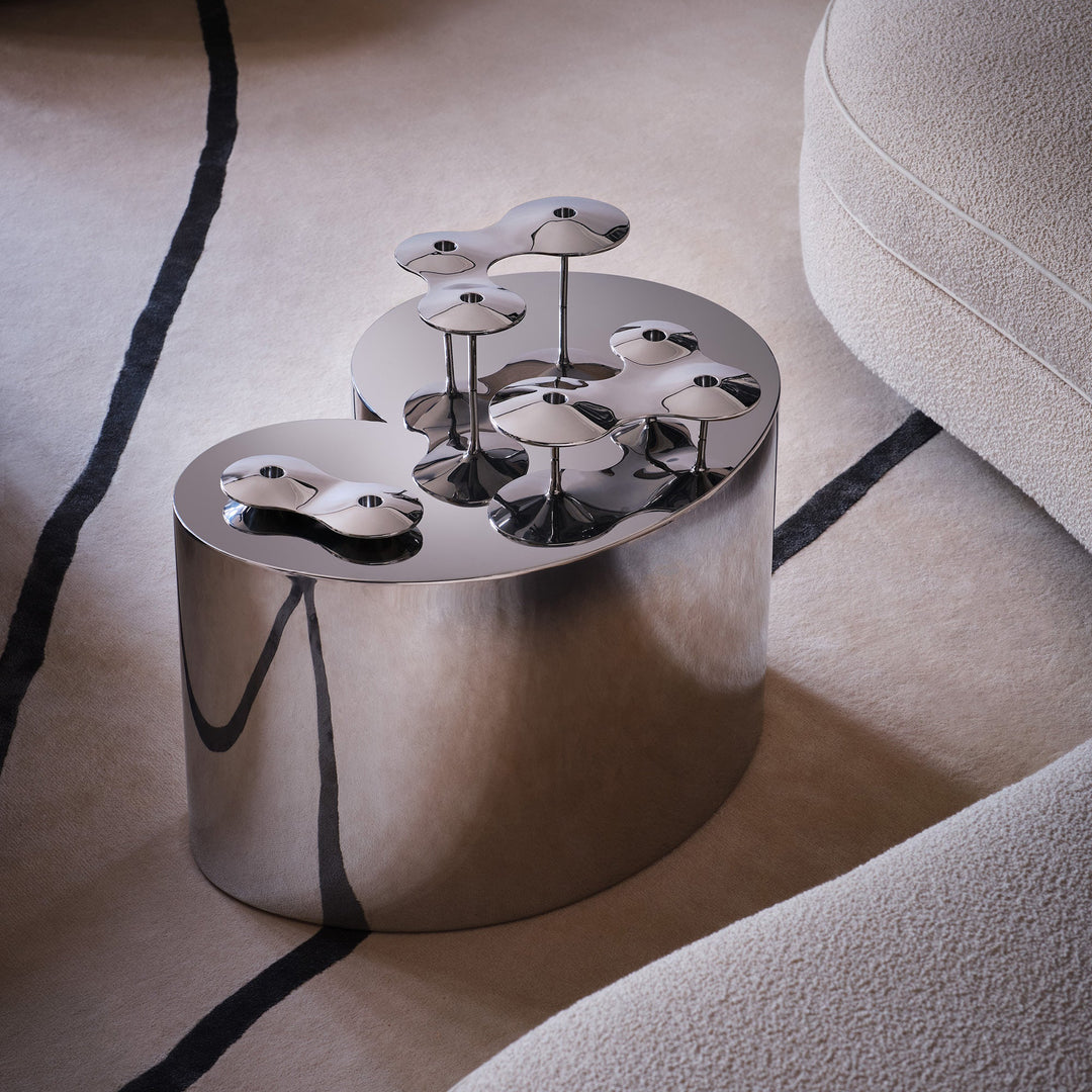 Cell Candle Holder — silver pieces in several sizes arranged on a polished steel side table beside a sofa