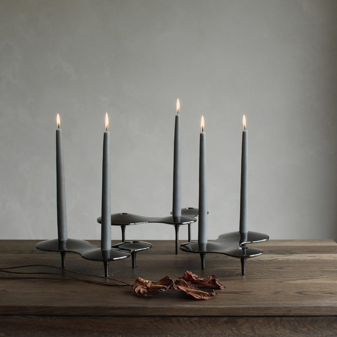 Cell Candle Holder — black pieces of several sizes holding lit grey tapered candles on a dark wood table