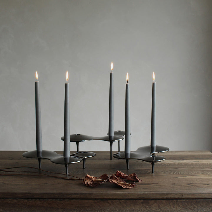 Cell Candle Holder — black pieces of several sizes holding lit grey tapered candles on a dark wood table