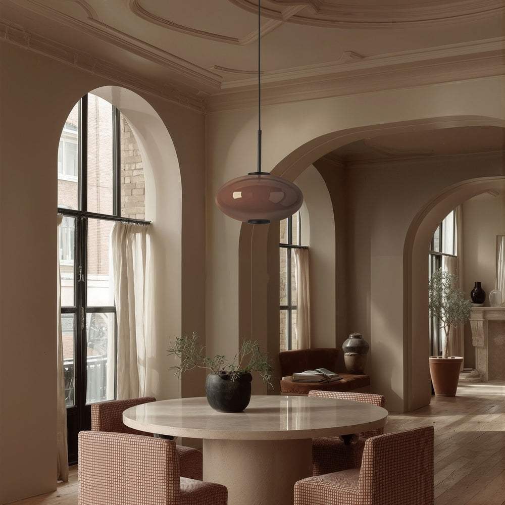 Ovalo Pendant Lamp in rose-tinted glass over a round stone dining table in an arched room