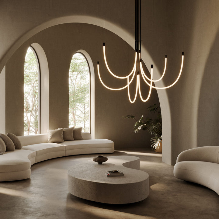 Cram Chandelier Chandelier in black lit above a curved white sofa and stone coffee table under arched windows