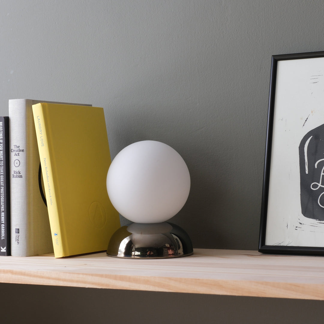 Frosted glass orb lamp with chrome base, styled beside books and art