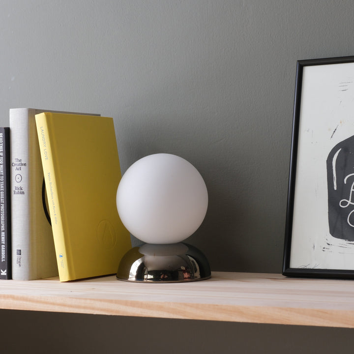 Frosted glass orb lamp with chrome base, styled beside books and art