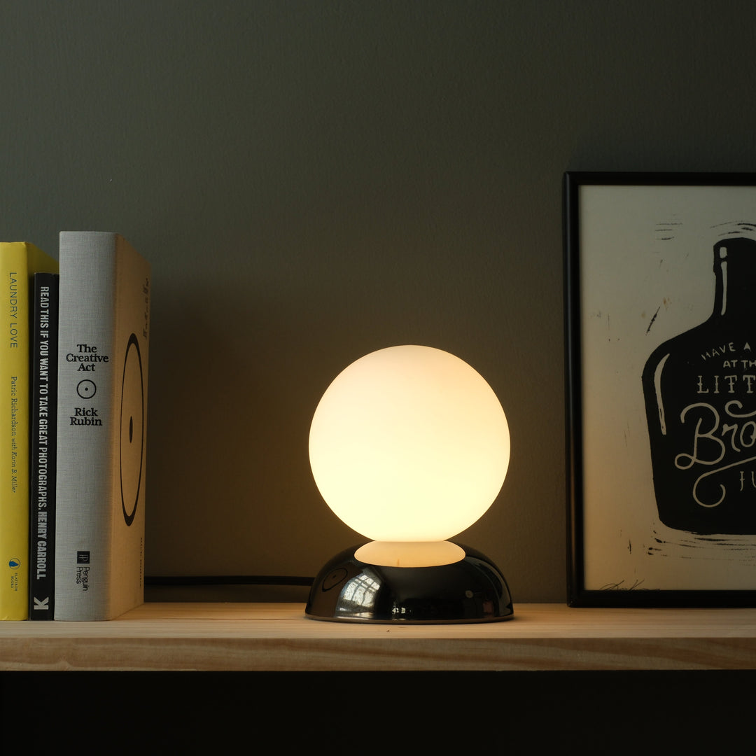 Globe table lamp with frosted glass shade and glossy black base, styled beside books and art