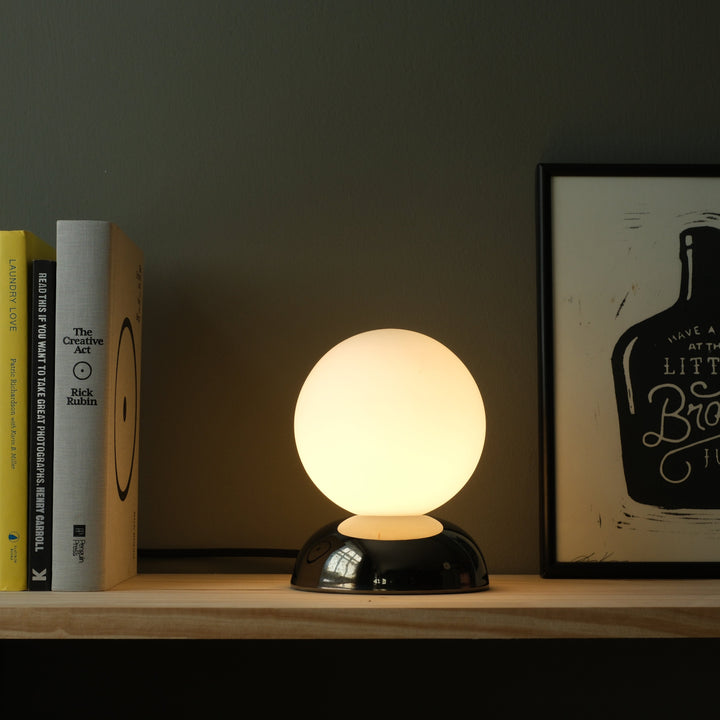Globe table lamp with frosted glass shade and glossy black base, styled beside books and art