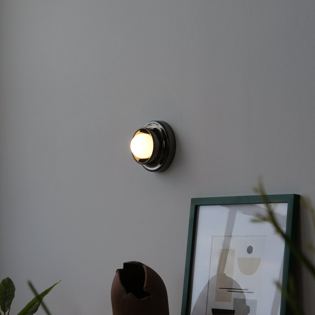 Sleek chrome wall sconce with warm glow, styled beside abstract art and ceramic vase