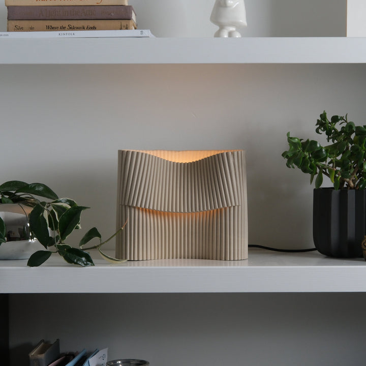 Rippled ceramic table lamp with warm glow, styled on shelf with greenery