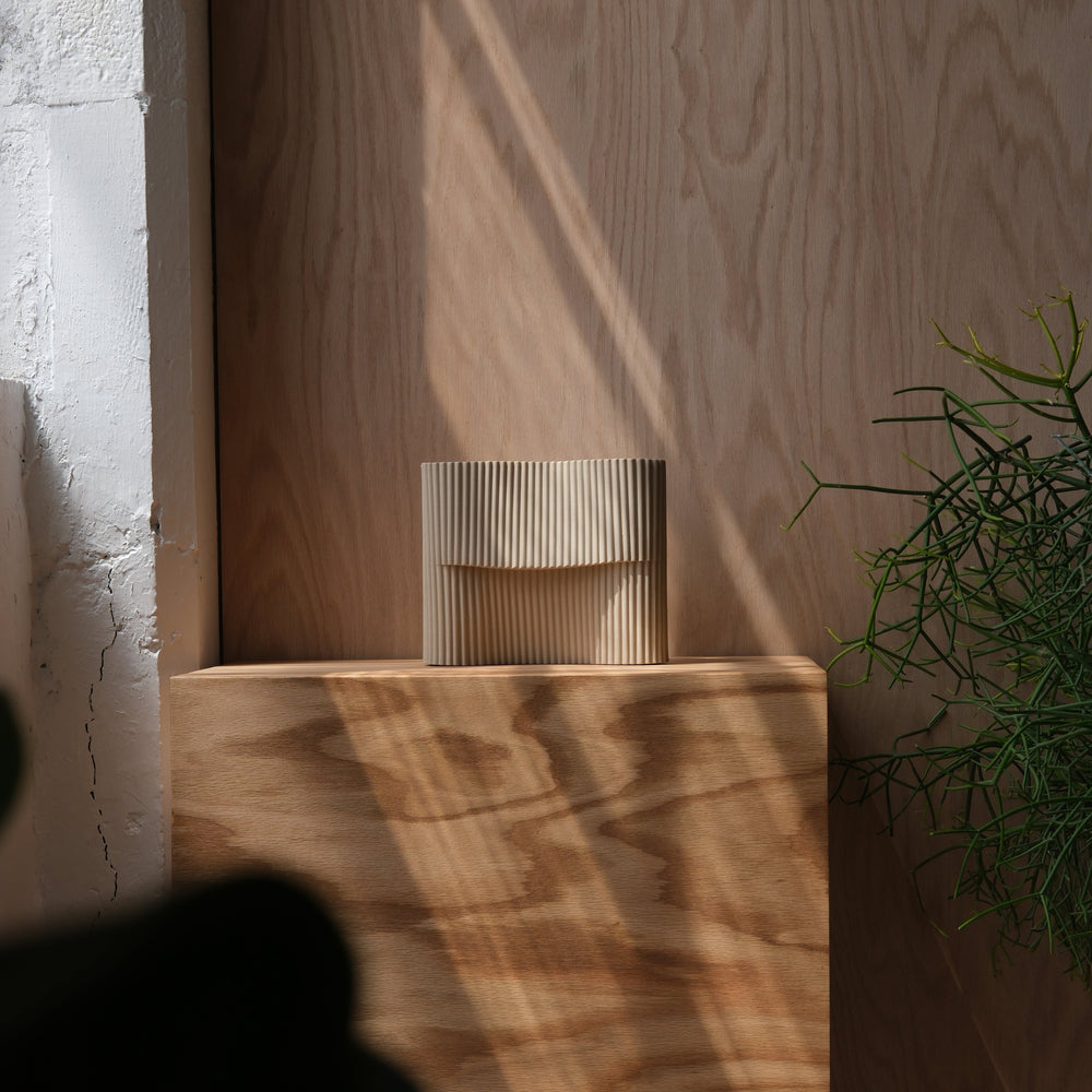 Rippled ceramic vase on natural wood pedestal, minimalist home decor
