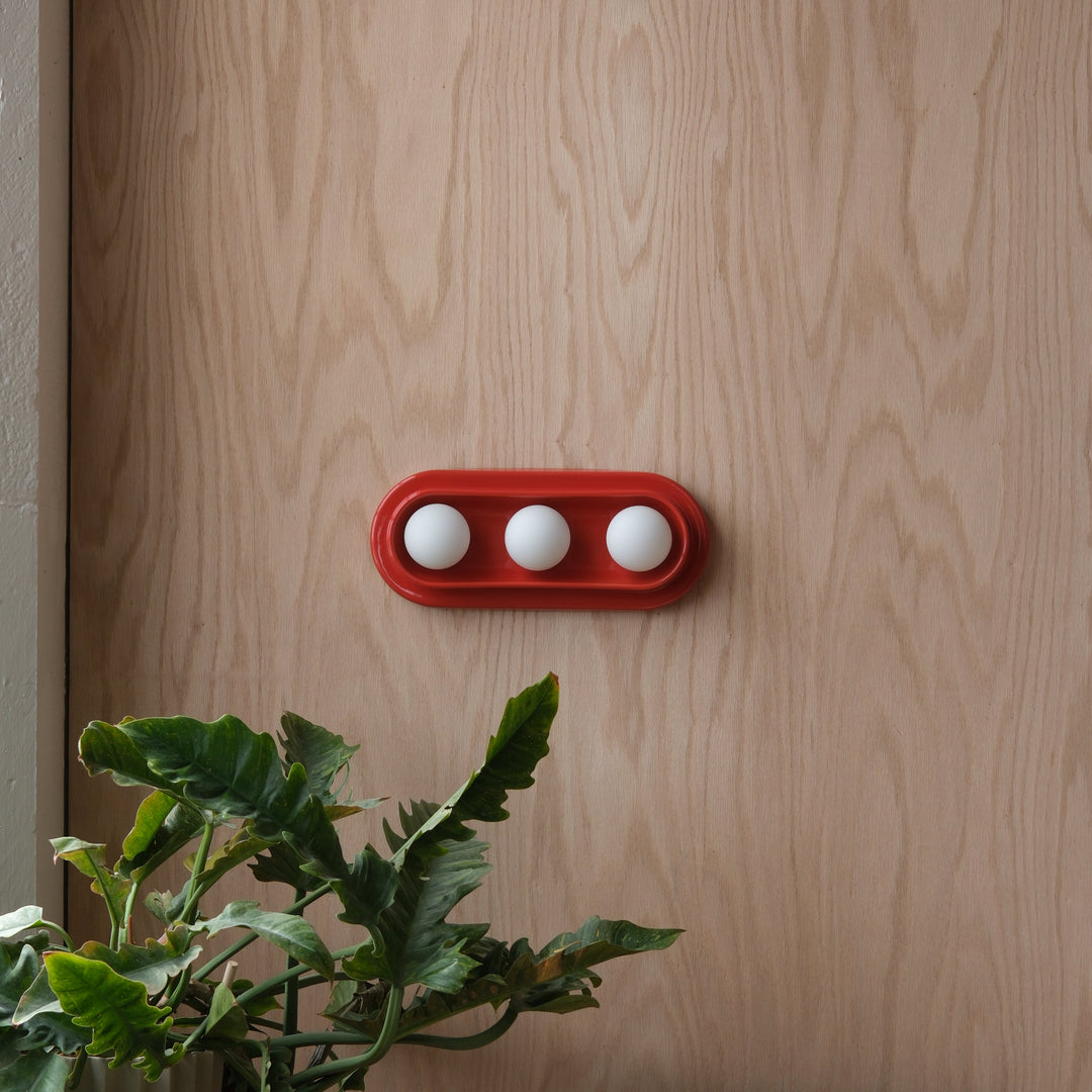 Red ceramic tray with white spheres, styled against wood backdrop with lush greenery