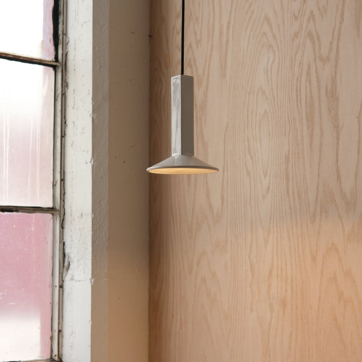 Ceramic pendant light with matte finish, suspended near wooden wall and vintage window