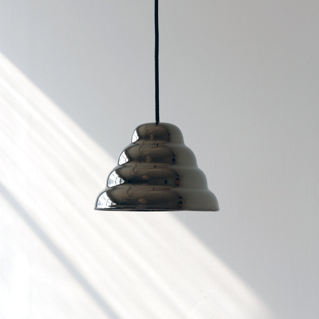 Sleek chrome pendant light with sculptural, tiered design against white wall, modern minimalist decor