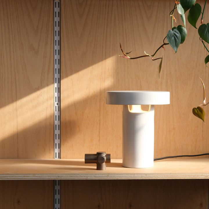 Modern white ceramic table lamp with minimalist design, paired with brass accent, on wooden shelf